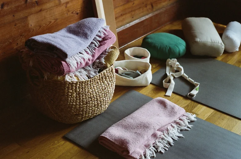 Basket of blankets, bolsters and straps beside yoga mats