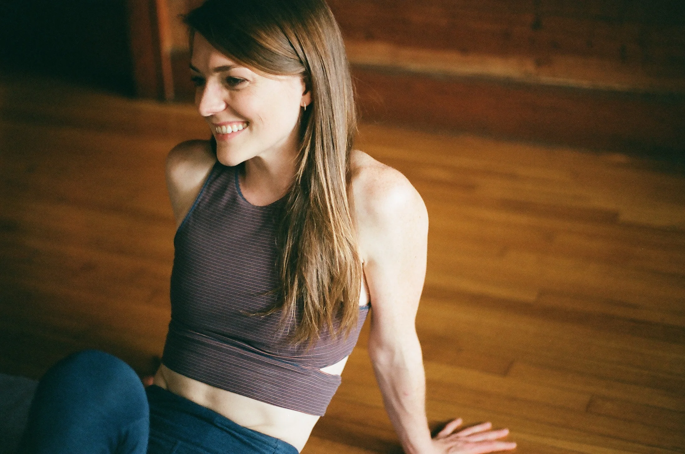 Yoga teacher smiling, seated on the wood studio floor