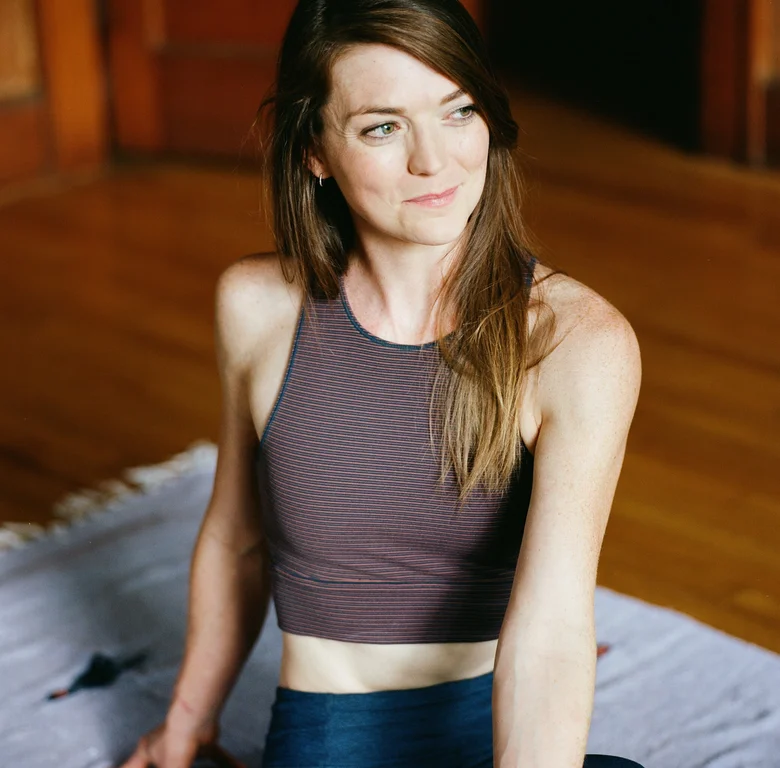 Yoga teacher seated on a woven rug